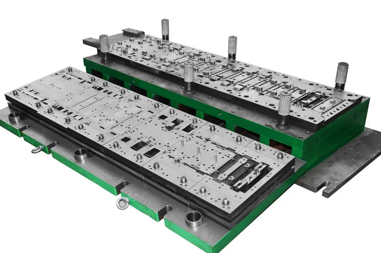 A large metal stamping die set with multiple components and cutouts, mounted on a green base, used for manufacturing and shaping sheet metal parts.