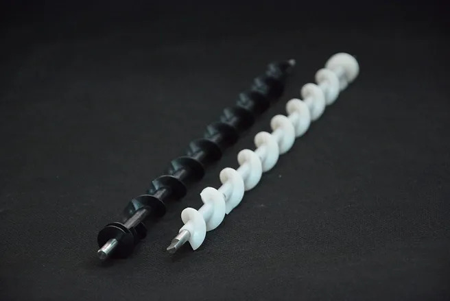 Two helical auger screws, one black and one white, are placed side by side on a black surface.